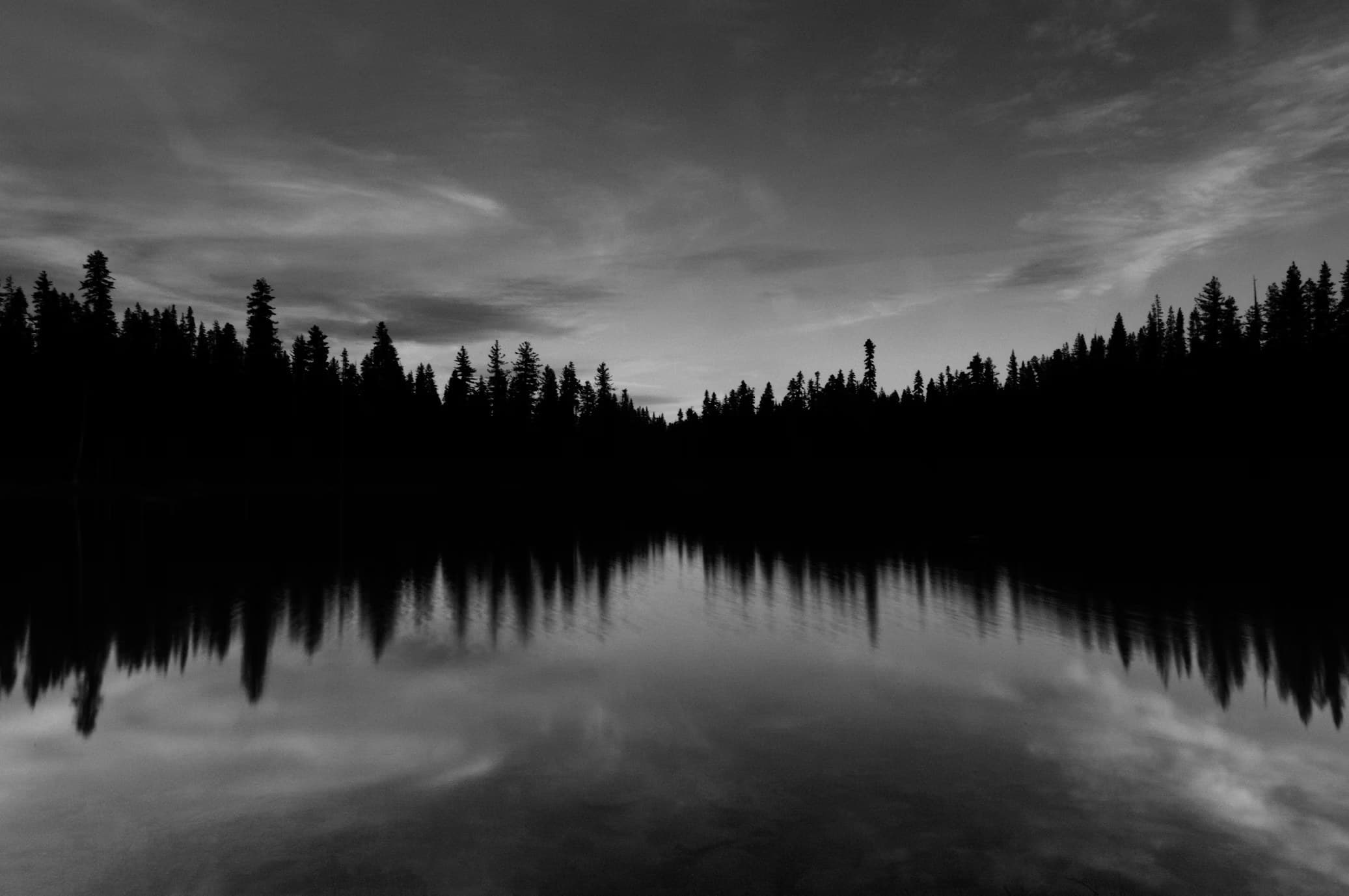 Lago ao entardecer refletindo a mata e o céu.